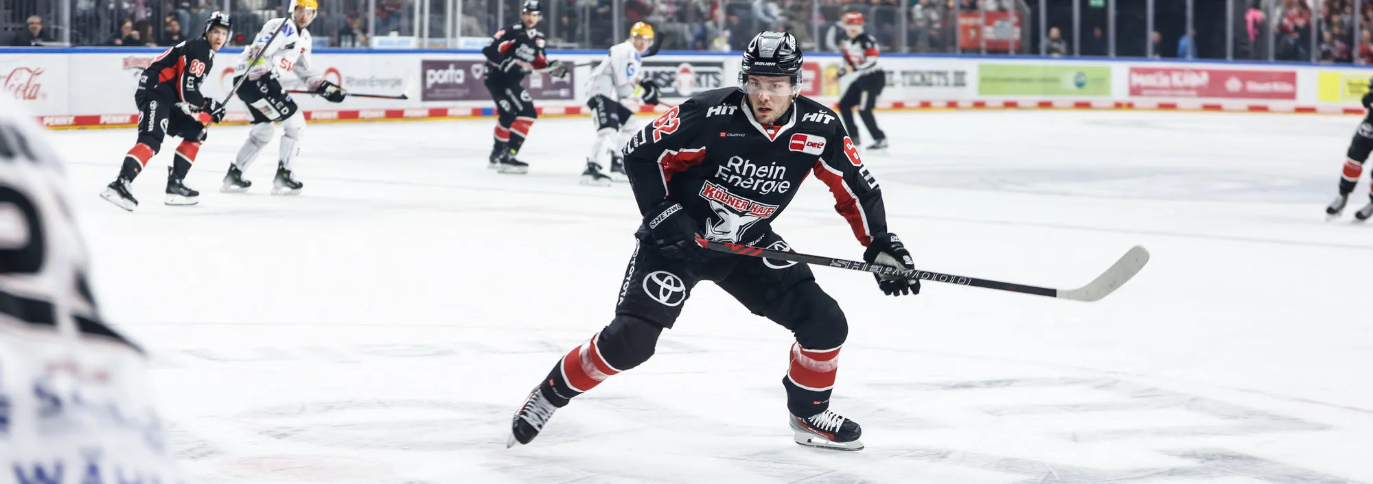 Un joueur de hockey sur glace portant un maillot noir et rouge patinant sur la glace avec un bâton de hockey.