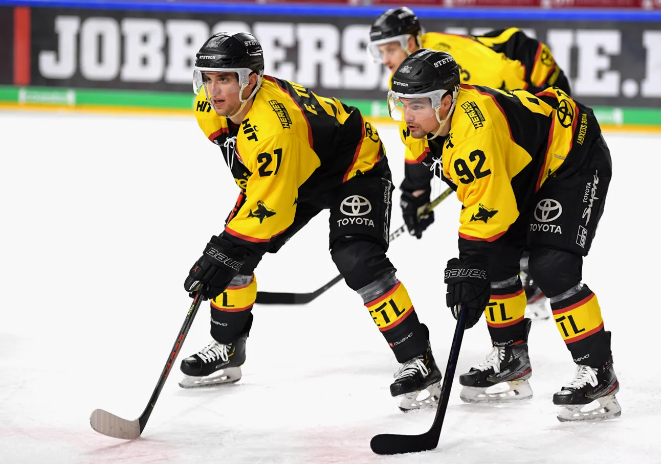 Deux joueurs de hockey sur glace en maillots jaunes et noirs avec les numéros 21 et 92 sur la glace, concentrés sur le jeu.