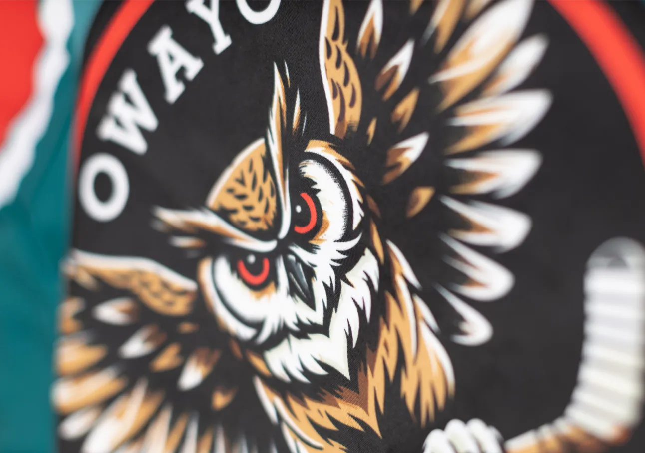 Une tête de hibou stylisée aux yeux rouges sur fond noir, entourée d'un cercle rouge et blanc, sur un vêtement de sport d'owayo.