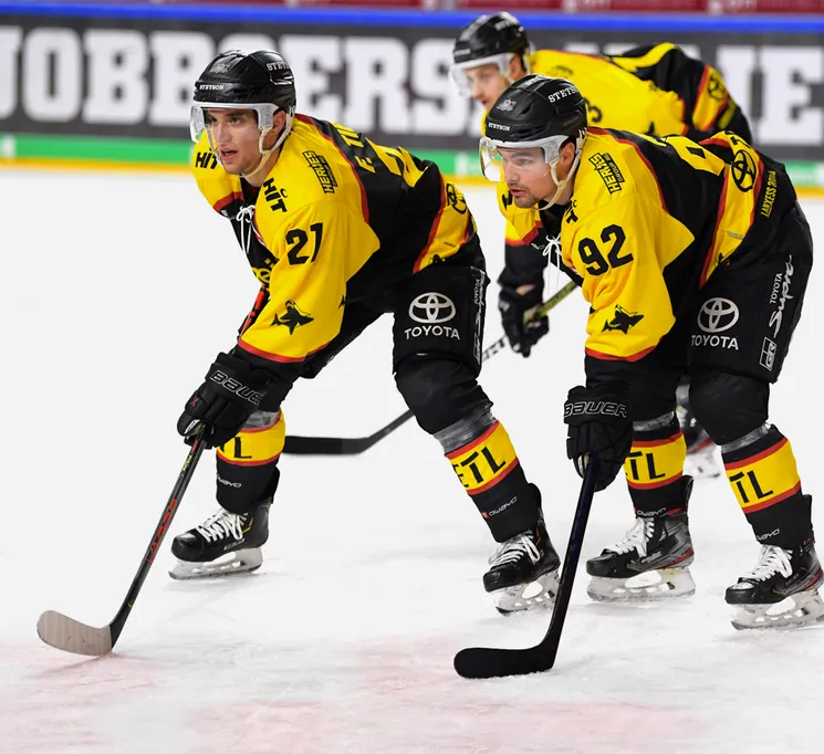 Joueurs de hockey sur glace en maillots jaunes et noirs avec les numéros 21 et 92 sur la glace, tenant leurs bâtons.