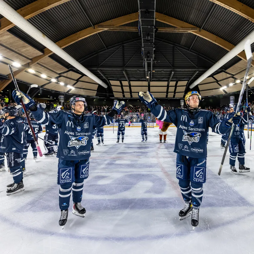 Deux joueurs de hockey sur glace sur la glace célébrant avec leurs bâtons tandis que d'autres joueurs et spectateurs sont visibles en arrière-plan.