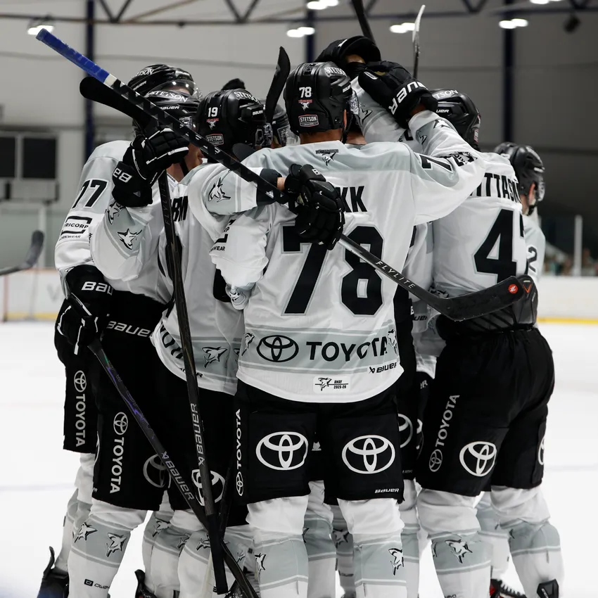Un groupe de joueurs de hockey sur glace en maillots blancs s'étreignent sur la glace après un but.