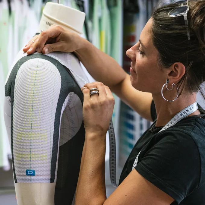 Une femme ajuste un vêtement de sport sur mesure sur un mannequin tout en portant un mètre ruban.
