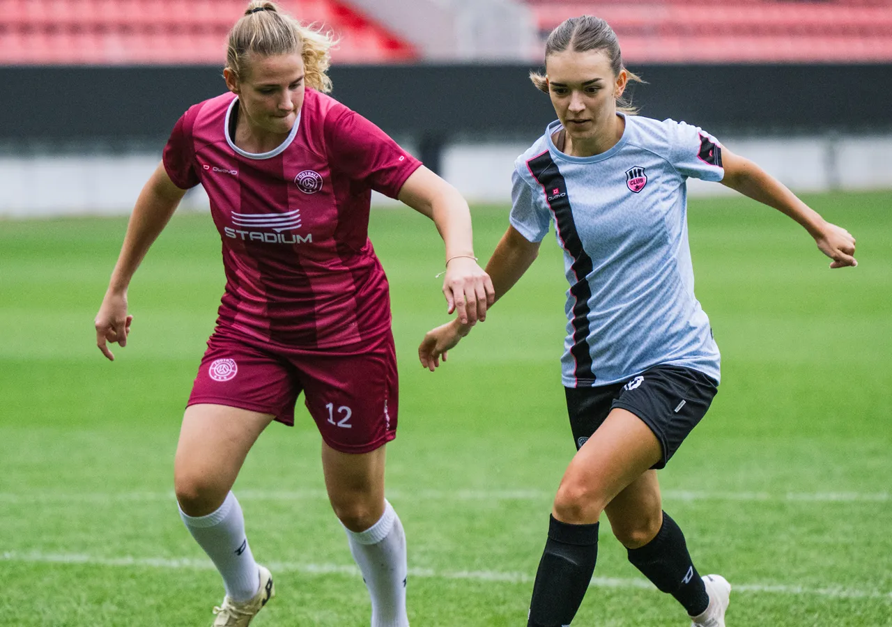 Deux footballeuses en maillots colorés interagissant sur un terrain en herbe.