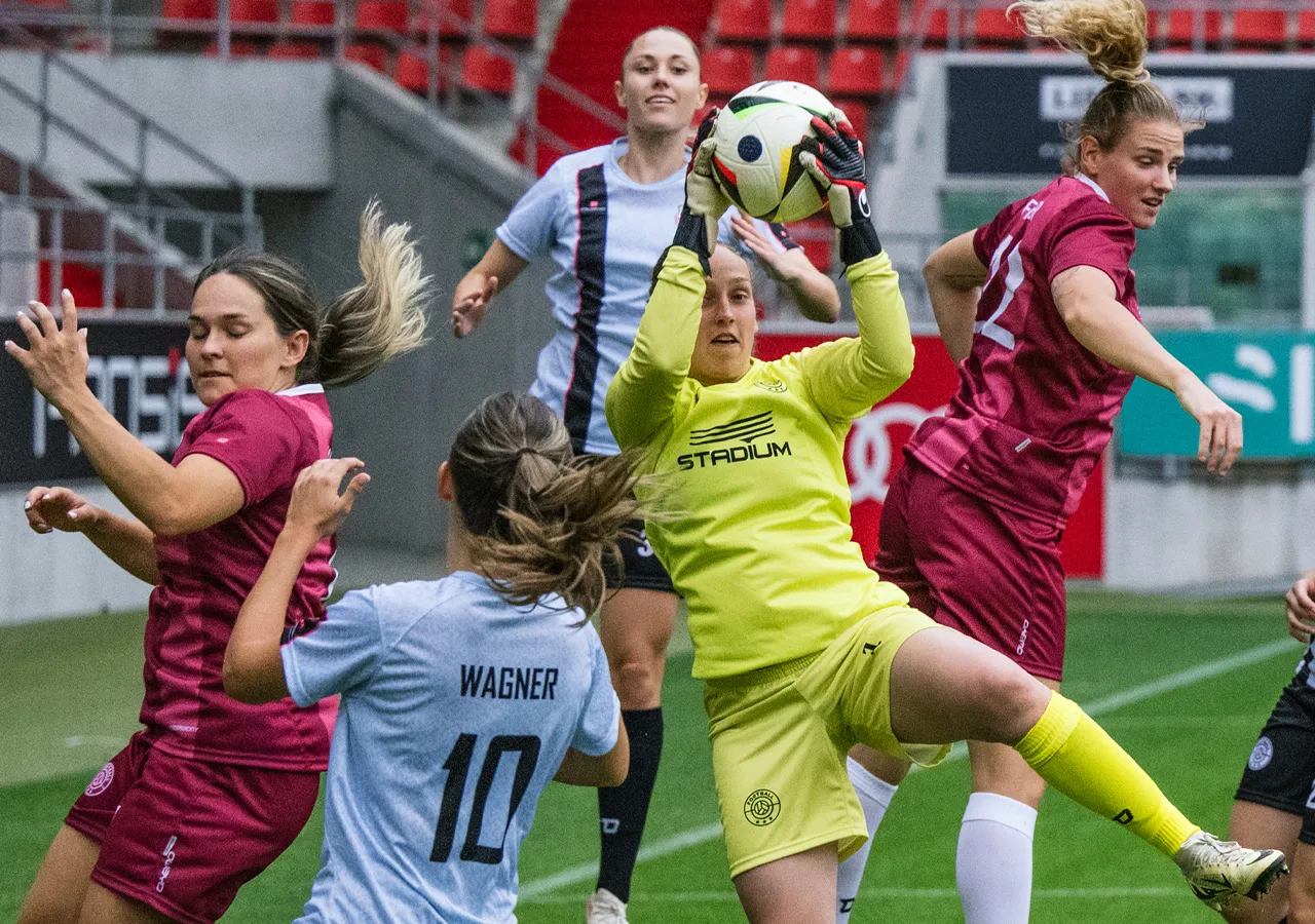 Une gardienne de but en tenue de sport jaune attrape un ballon de football pendant que d'autres joueuses en maillots différents se battent pour le ballon.