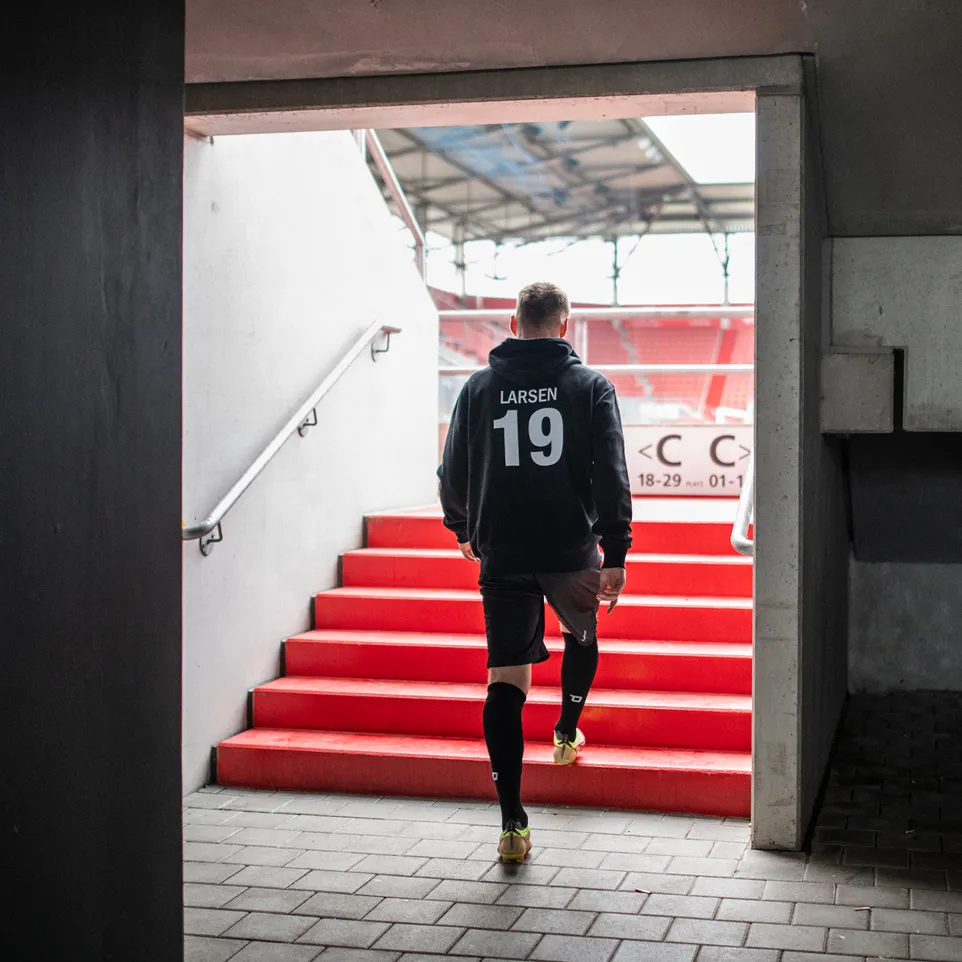 Un athlète portant un sweat à capuche noir et un short monte un escalier rouge dans un stade.