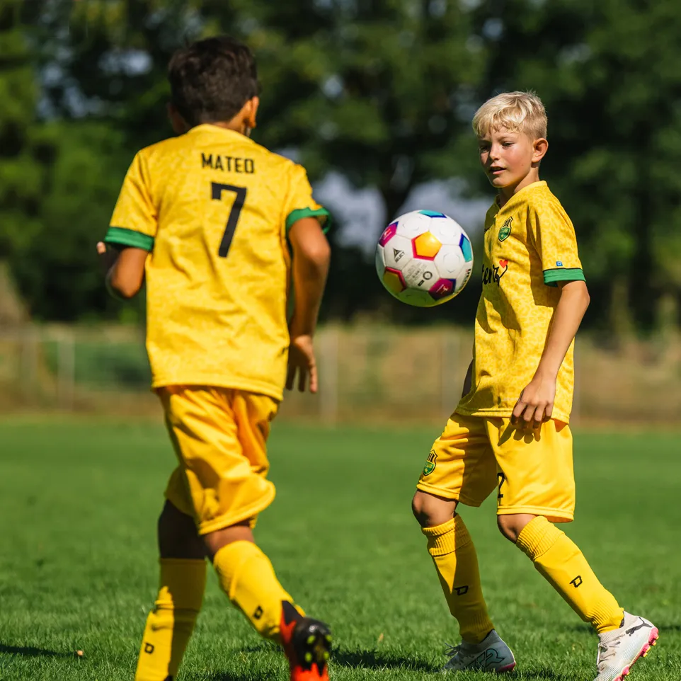 Deux enfants en maillots de football jaunes et en shorts jouent sur un terrain de football vert.