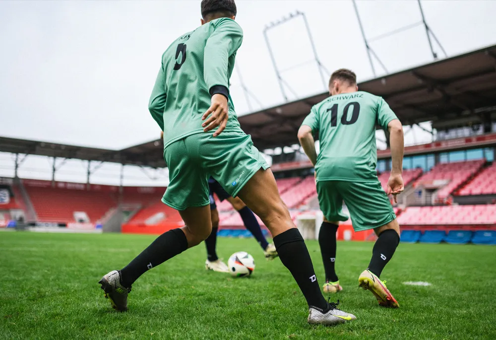 Deux joueurs de football en maillots verts et chaussettes noires jouant sur un terrain en herbe.