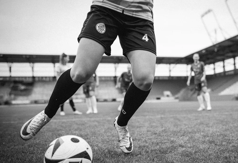 Une joueuse en short de football court et en chaussettes longues dribble un ballon sur le terrain.