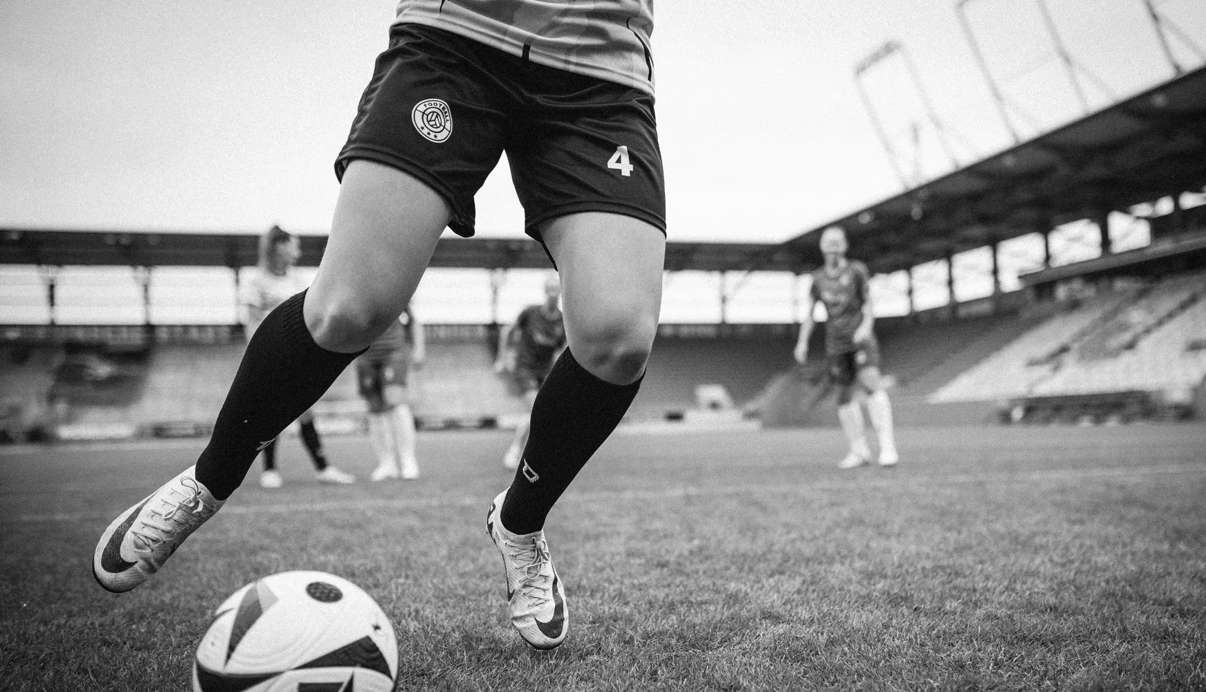 Une joueuse en shorts de football courts et en chaussettes longues frappe un ballon sur un terrain de football.