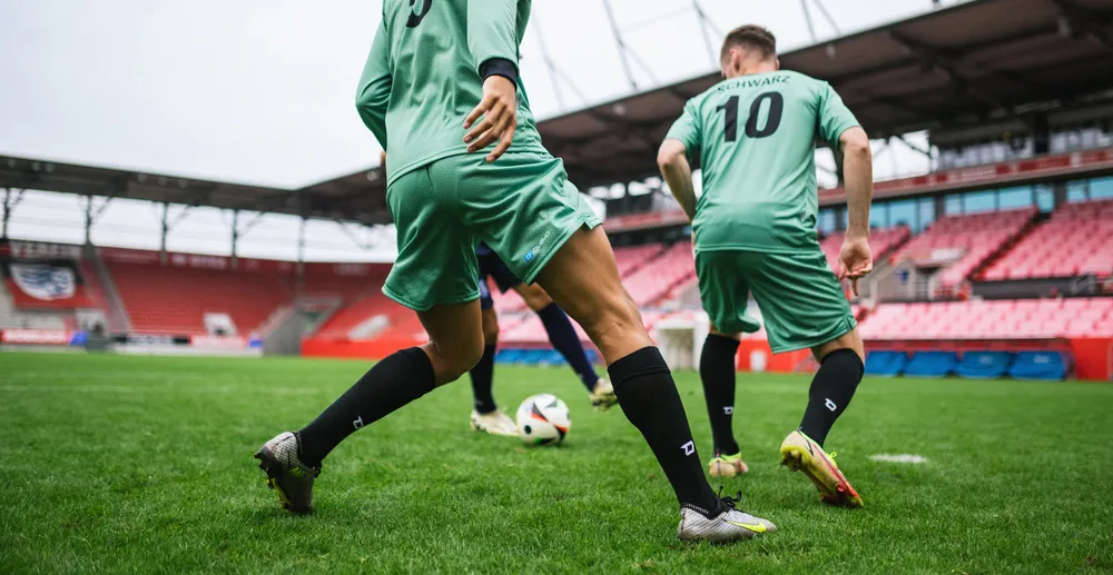 Deux joueurs de football en maillots vert clair et chaussettes noires s'entraînent sur un terrain en gazon dans un stade.