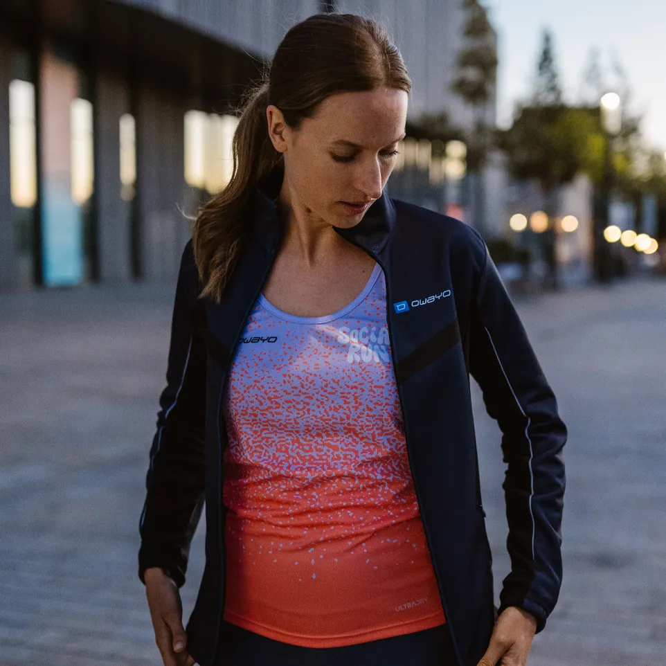 Une femme porte une veste sportive et un haut sans manches coloré avec un design moderne, tout en se tenant sur une rue urbaine.