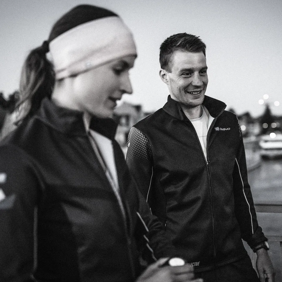 Deux athlètes en vestes noires modernes se tiennent à l'extérieur, souriant et prêts pour l'entraînement.