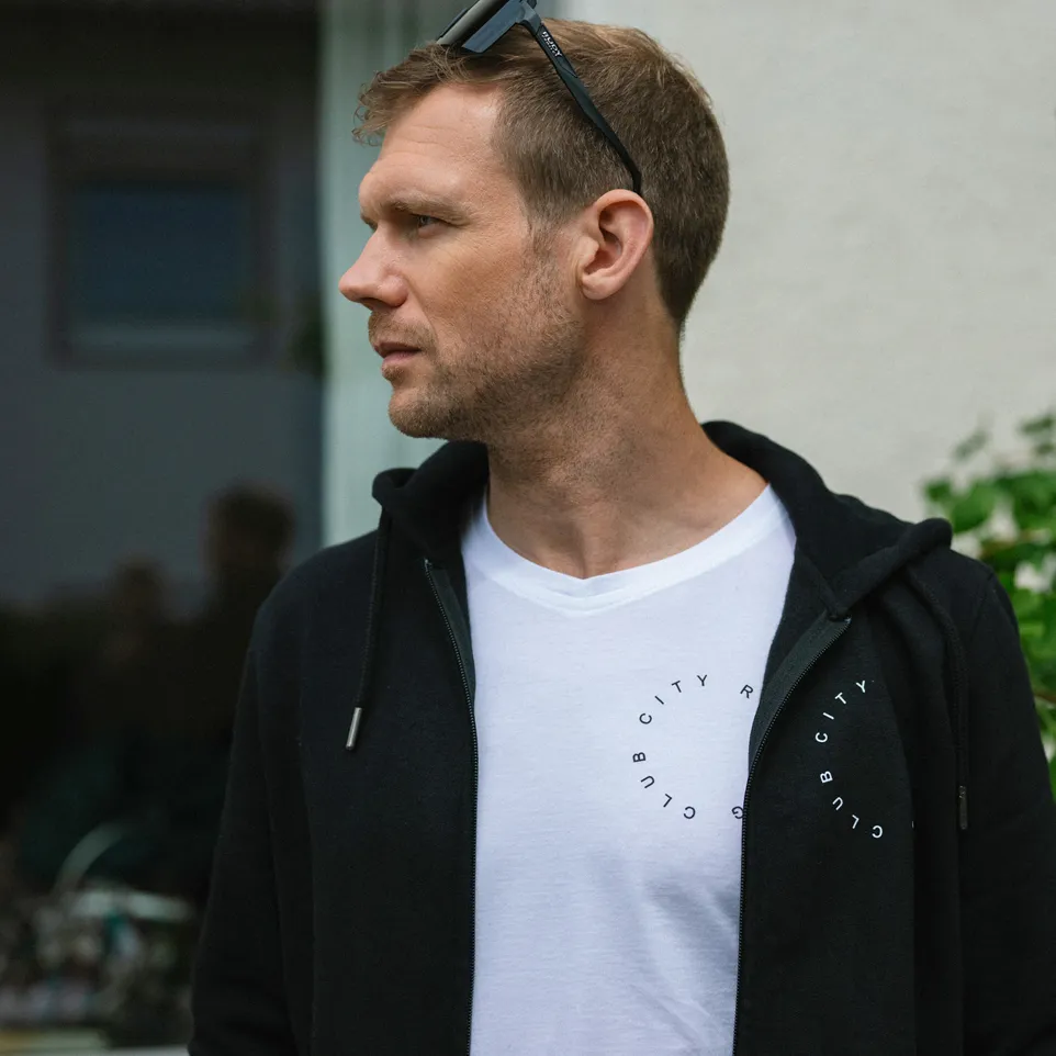 Un homme porte un sweat à capuche noir sur un t-shirt blanc avec un imprimé circulaire.