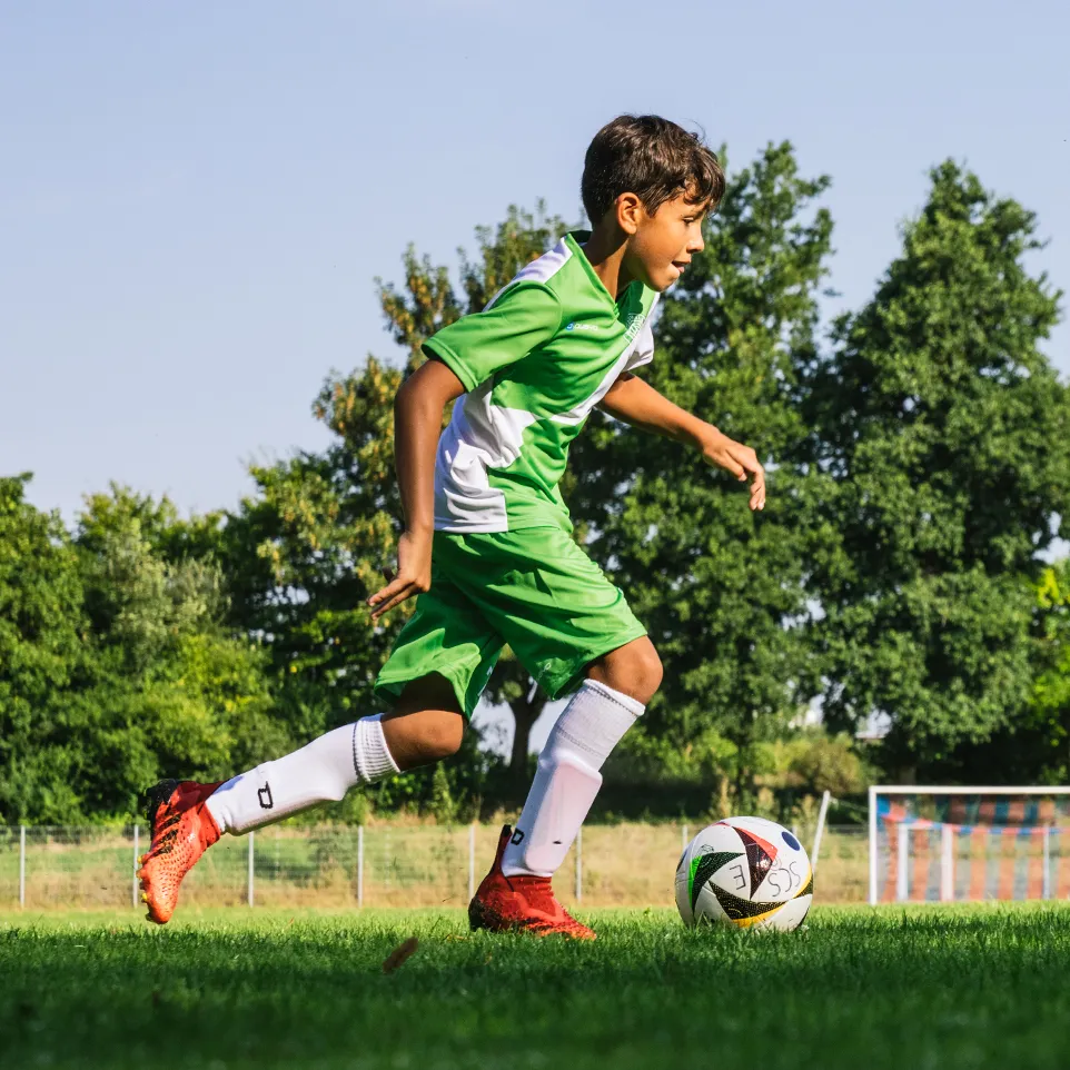Un jeune footballeur en tenue de sport verte et blanche court sur un terrain de football.