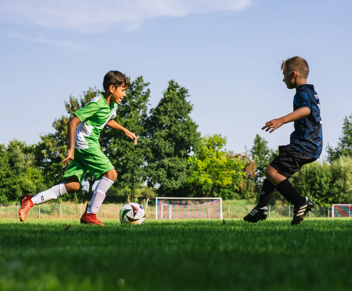 Un jeune joueur de football en maillot vert court avec le ballon sur un terrain gazonné.