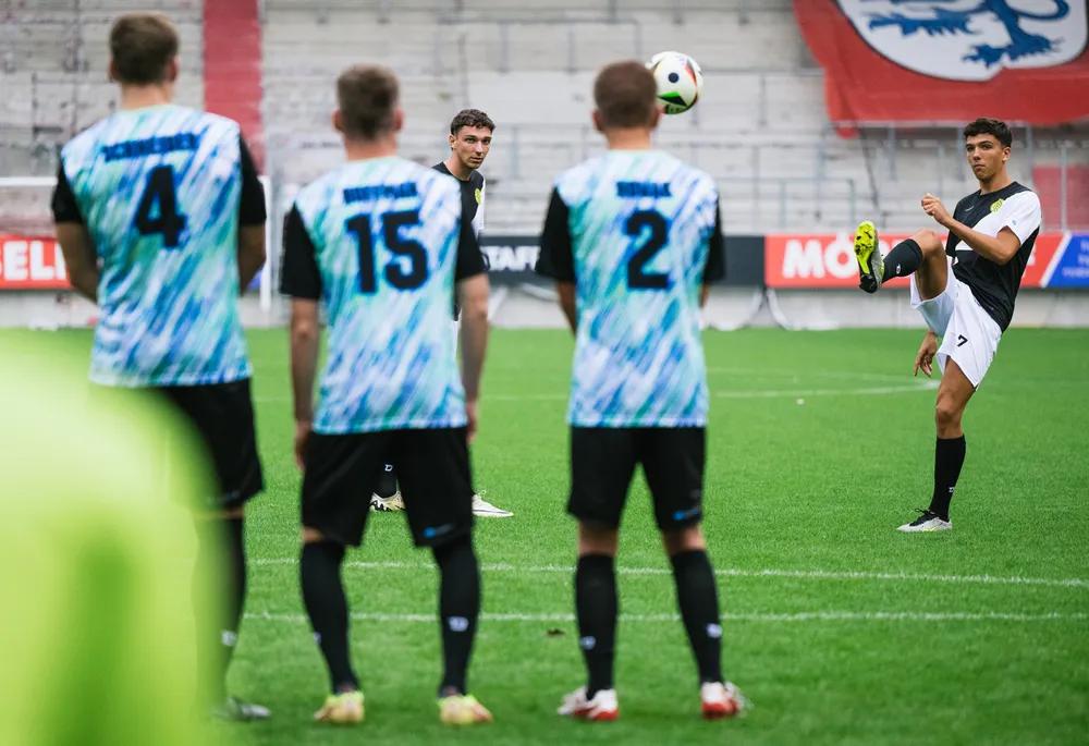 Un groupe de footballeurs en maillots colorés se tient sur le terrain pendant qu'un joueur se prépare à tirer un coup franc.