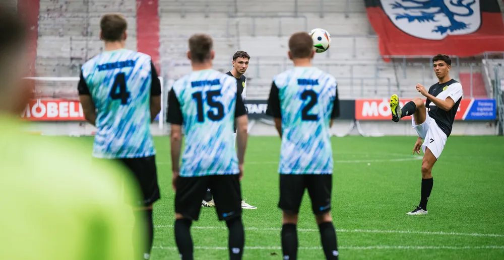 Un joueur de football effectue un tir pendant que d'autres joueurs en maillots colorés regardent.