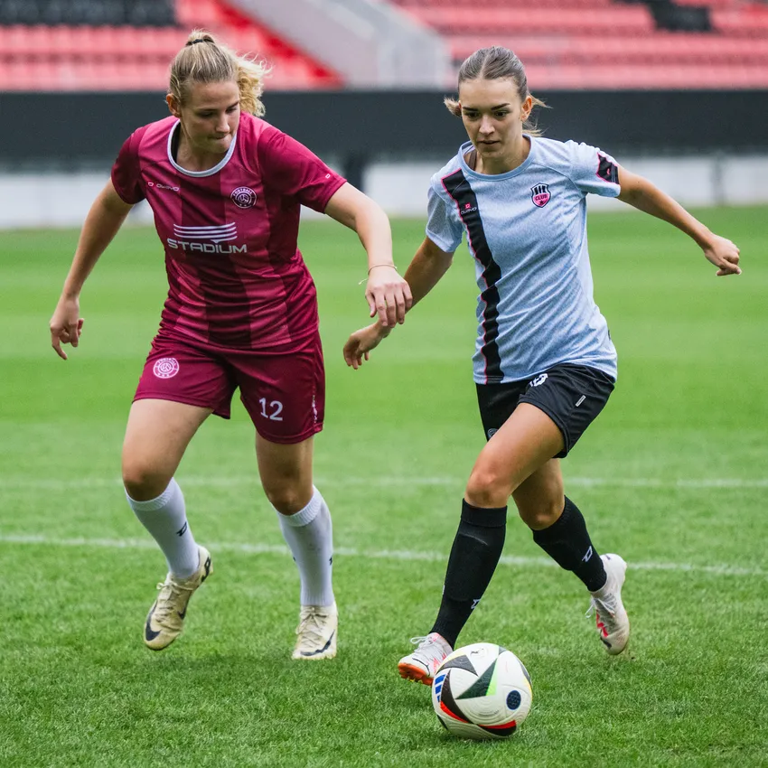 Deux femmes en tenue de sport jouent au football sur un terrain vert.