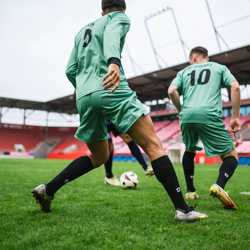 Deux joueurs de football en maillots verts et chaussettes noires jouant sur un terrain en herbe avec un ballon.