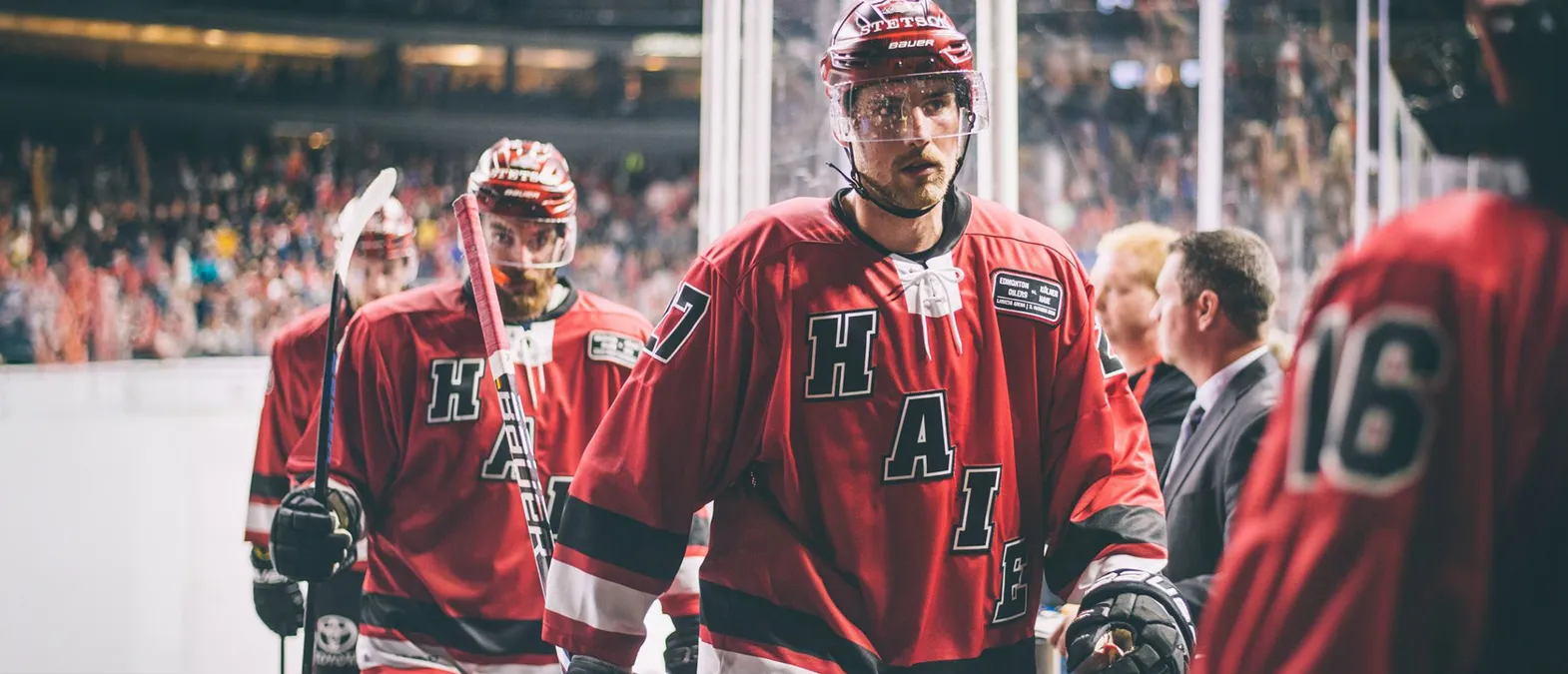 Joueurs de hockey sur glace en maillots rouges avec les lettres 'H', 'A', 'I', 'E' et le numéro 7 dans le dos, debout sur la glace.
