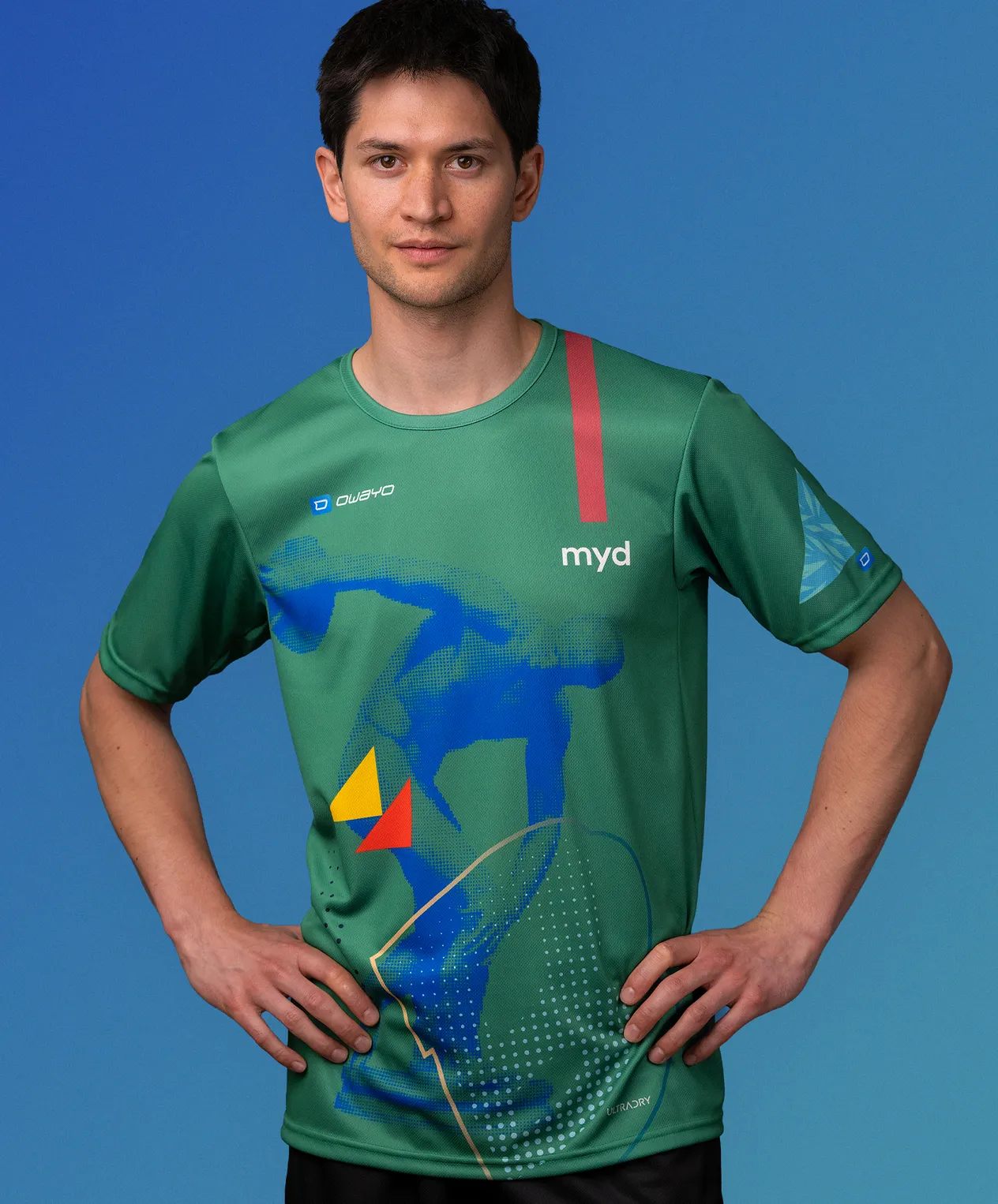 Un homme portant un maillot de sport vert personnalisé de owayo avec un motif graphique bleu, jaune et rouge et l'inscription 'myd' sur la poitrine.