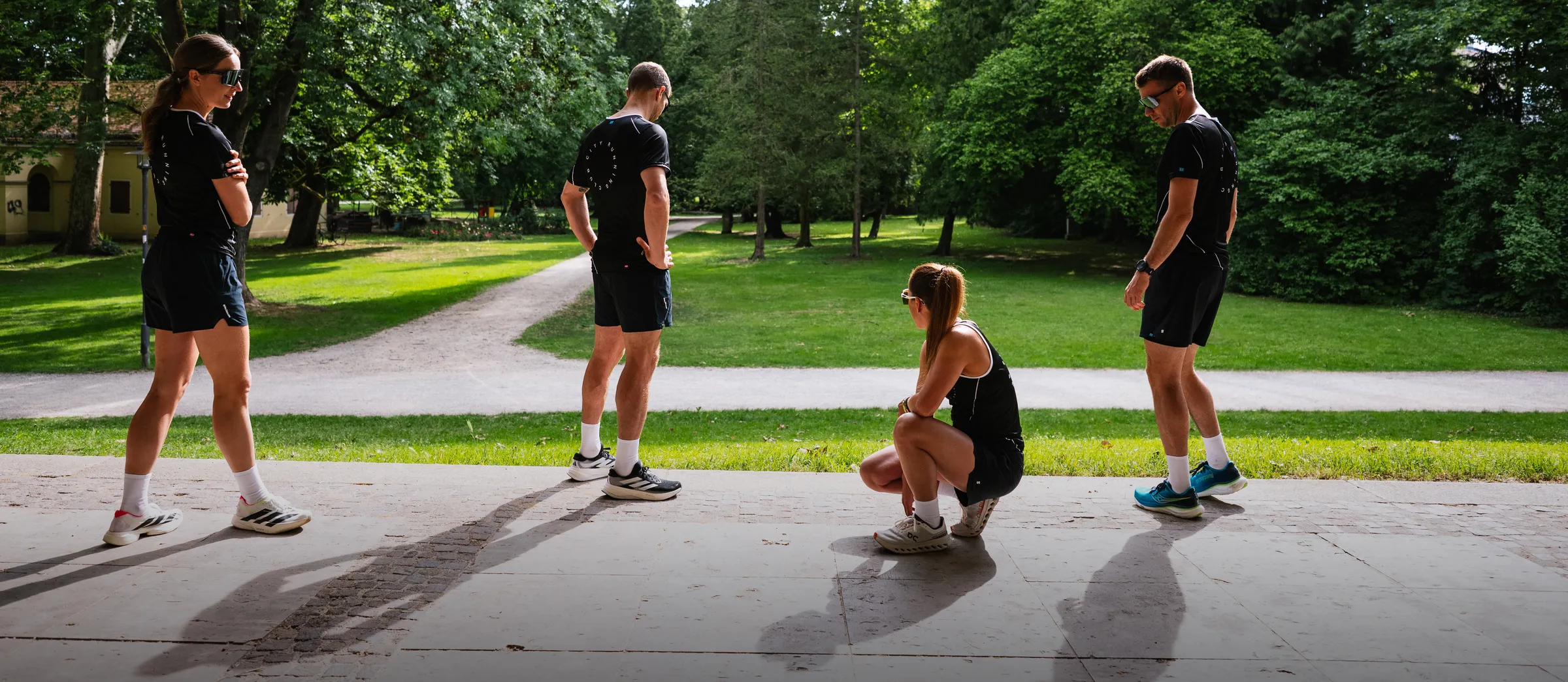 Quatre personnes en vêtements de sport se tiennent et s'asseyent dans un paysage de parc verdoyant.