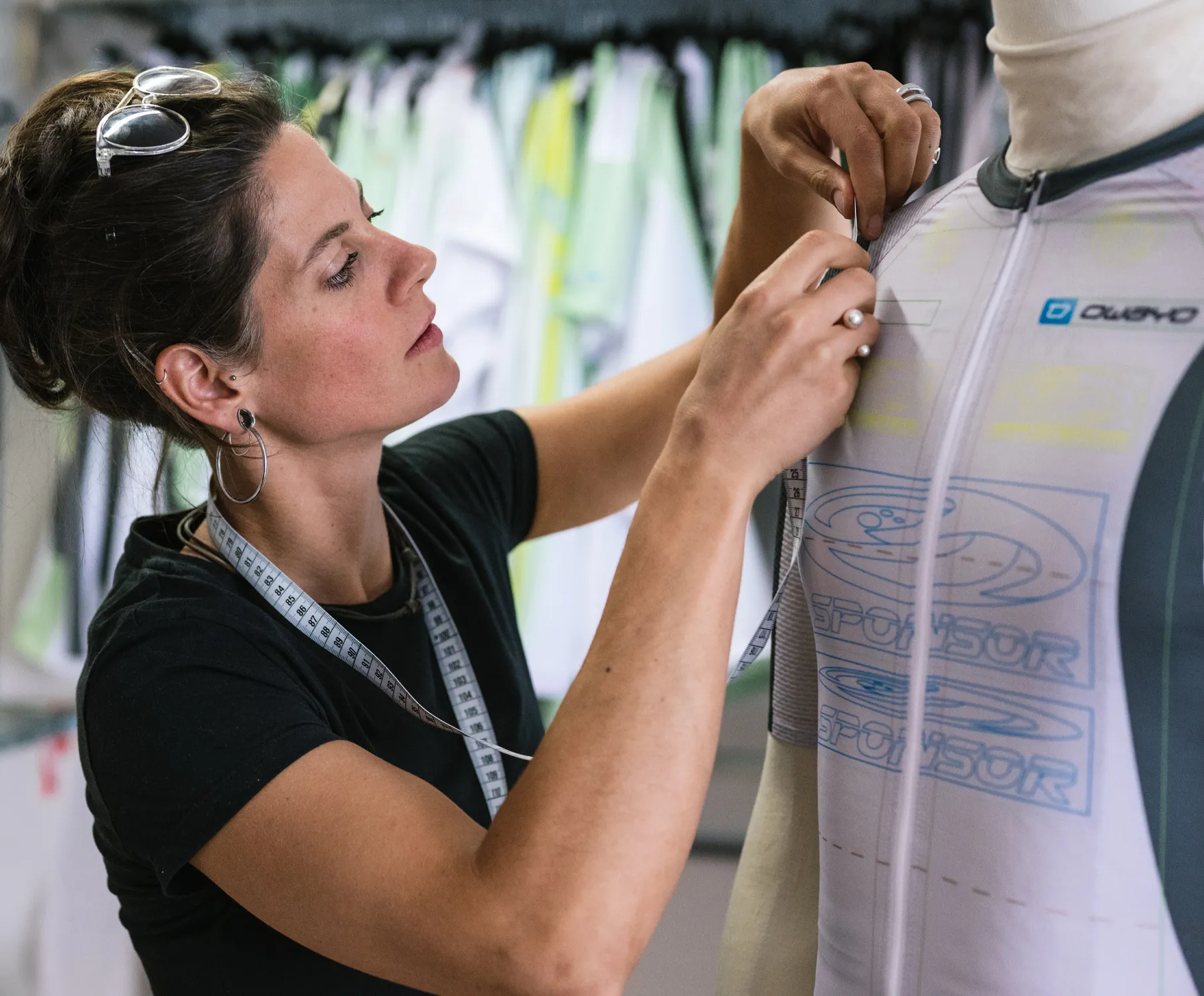 Une femme ajuste un maillot de sport personnalisé sur un mannequin, portant un mètre ruban autour du cou.