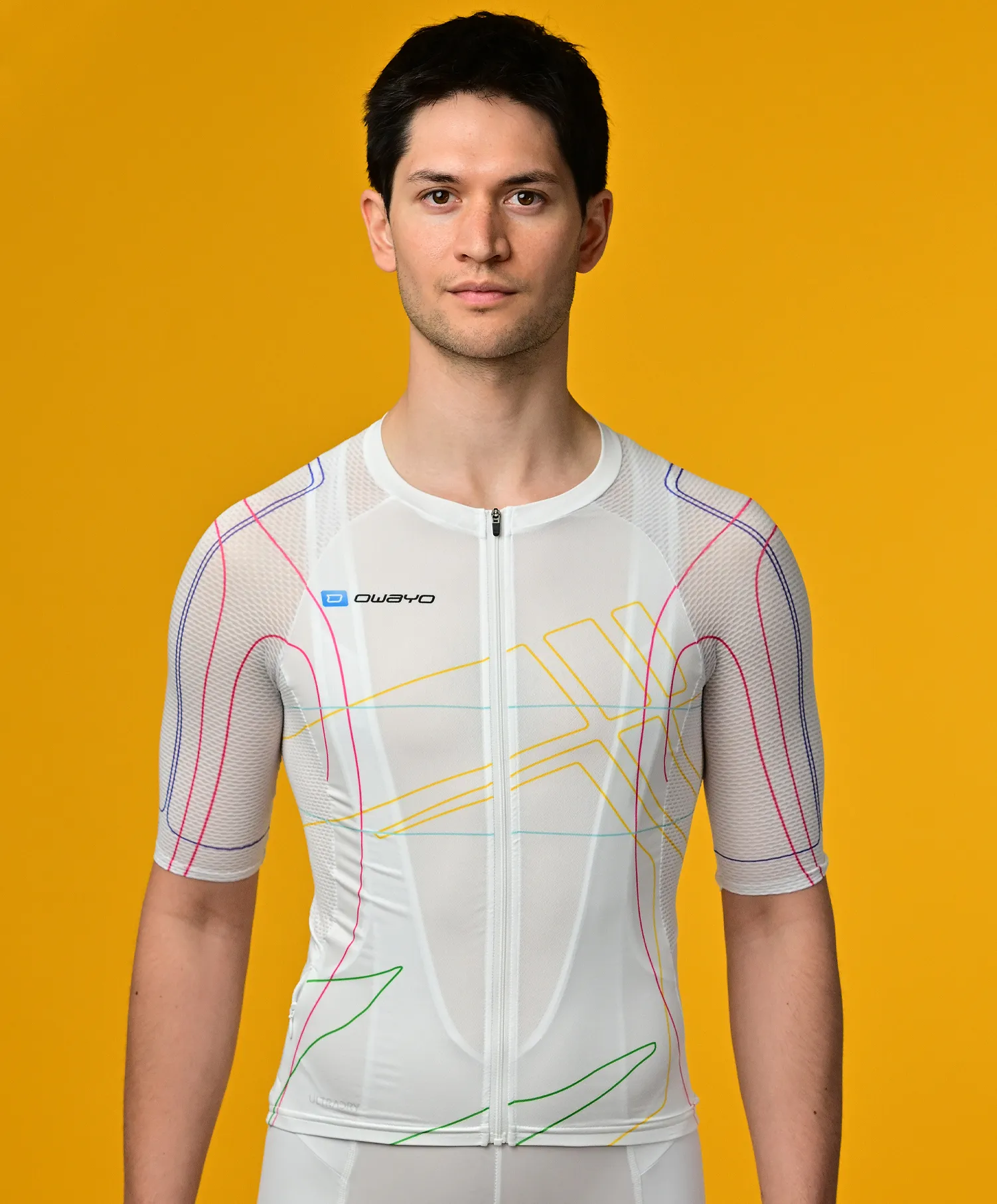 Un homme porte un maillot sportif blanc à manches courtes avec des lignes colorées de owayo devant un fond jaune.