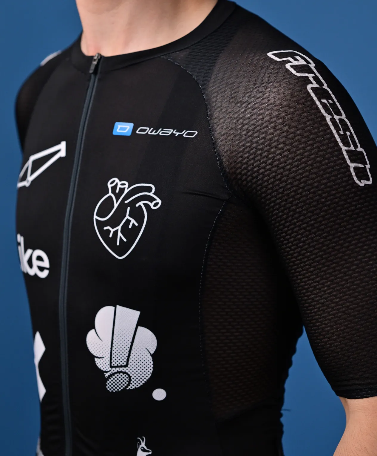 Une personne porte un maillot de sport noir sans manches de owayo avec une fermeture éclair devant, orné de divers logos et graphismes blancs, notamment un cœur et un 'O' stylisé, sur la poitrine et la manche.