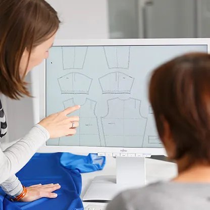 Deux personnes regardent des modèles numériques de vêtements de sport sur un écran d'ordinateur, l'une pointant vers l'écran.