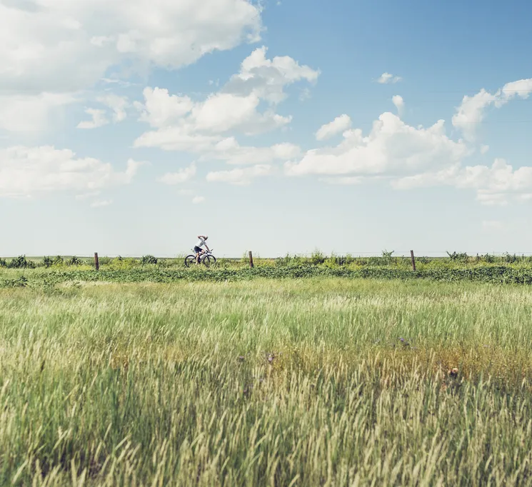 Un cycliste dans un paysage rural avec de l'herbe haute et un ciel bleu, symbolisant la responsabilité écologique et les activités de plein air.
