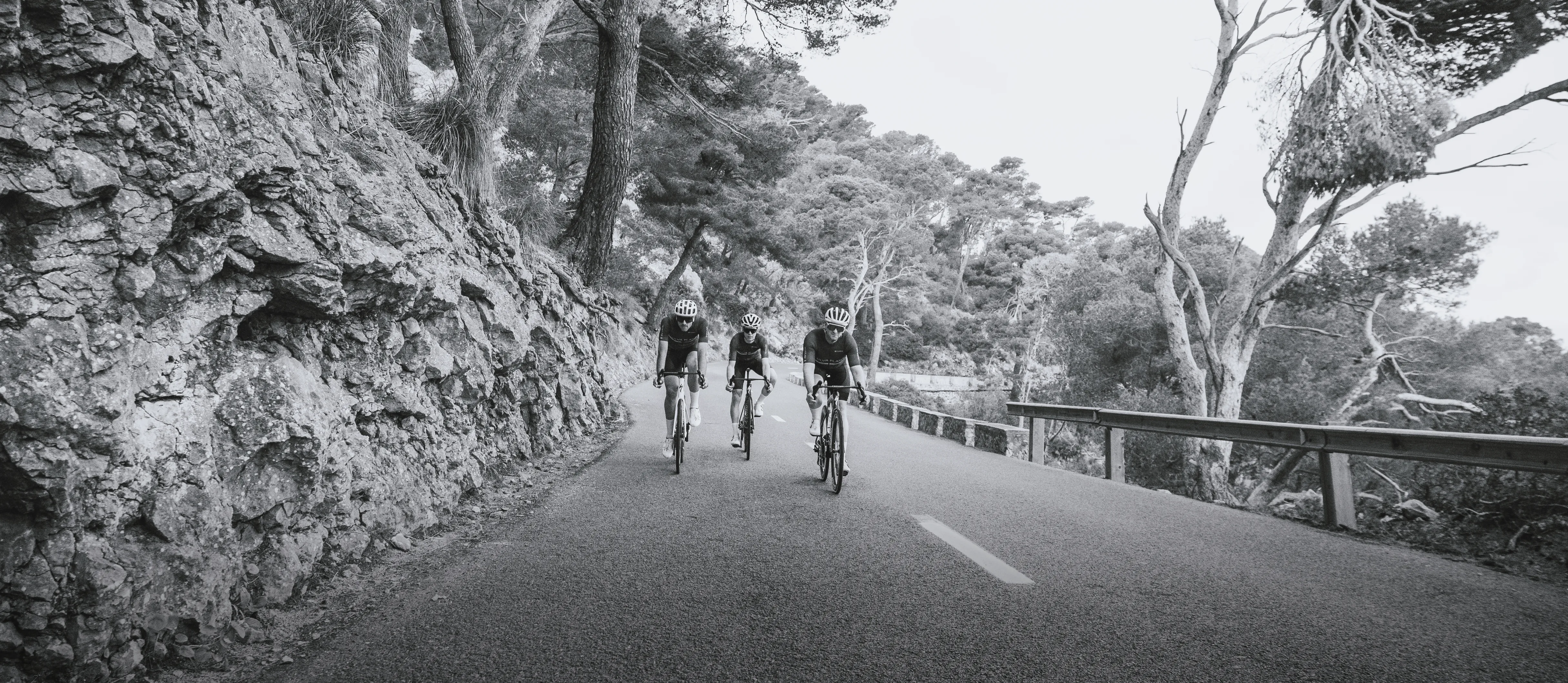 Trois cyclistes en vêtements de sport roulent sur une route le long d'une falaise rocheuse.