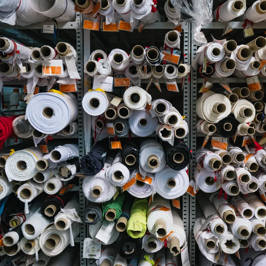 Étagères remplies de rouleaux de tissu de différentes couleurs et tailles, utilisés pour la fabrication de vêtements de sport.