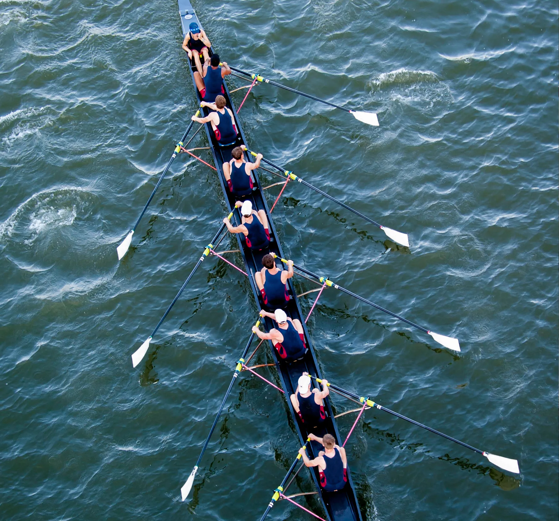 Un groupe de rameurs en vêtements de sport assortis rame en synchronisation sur un plan d'eau.