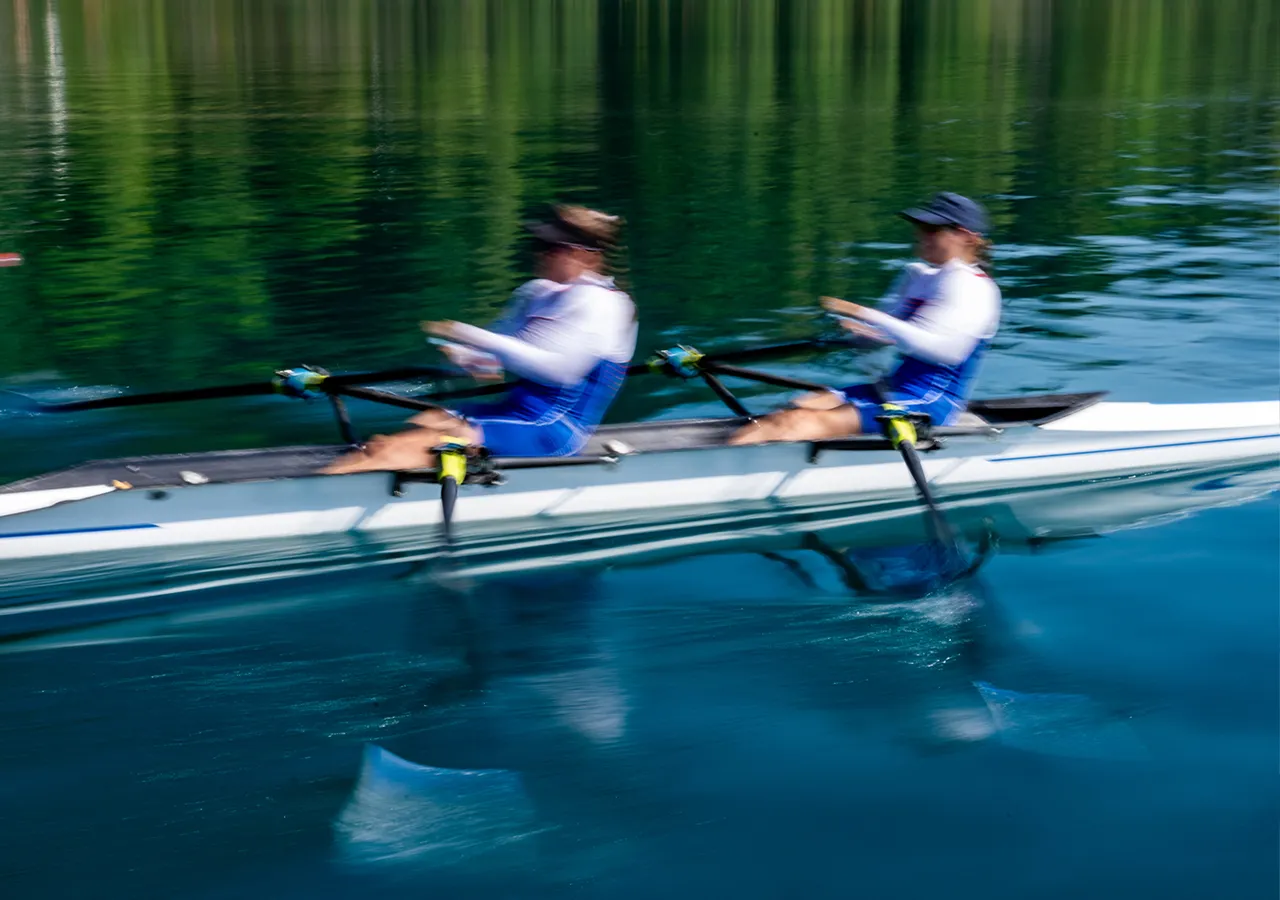 Deux rameurs en vêtements de sport bleus rament en synchronisation sur une surface d'eau calme.