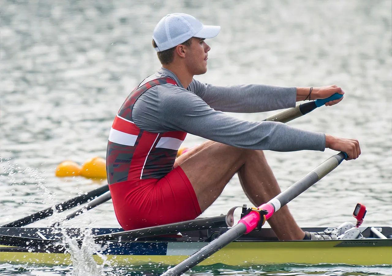 Un rameur en tenue de sport rouge et grise rame sur un plan d'eau.