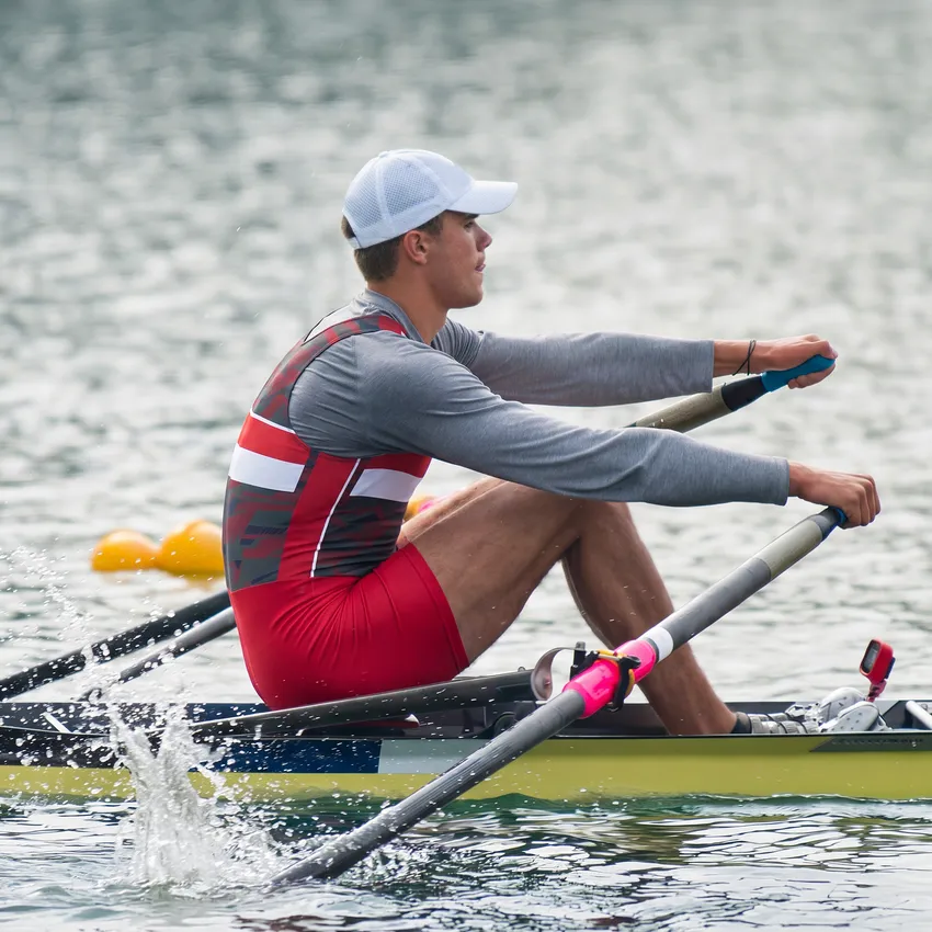 Un rameur en tenue de sport rouge et grise rame sur un plan d'eau.