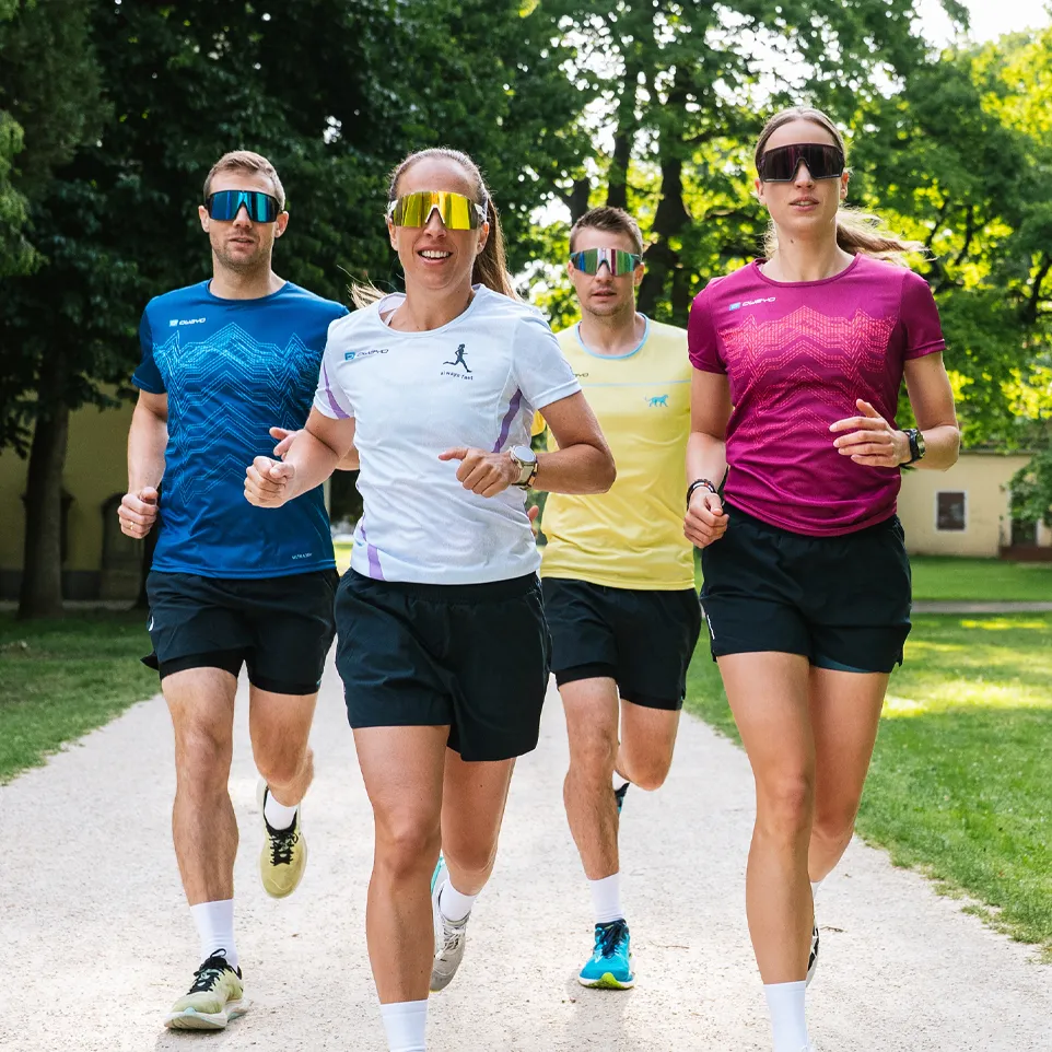 Quatre coureurs portant des t-shirts de sport colorés et des shorts courent sur un chemin dans un parc.