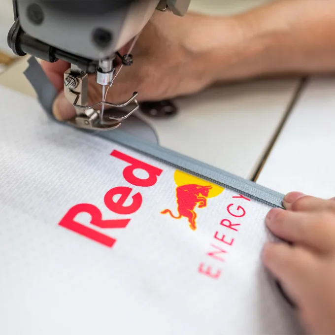 Un gros plan d'une machine à coudre qui brode un vêtement sportif blanc avec le logo Red Bull, tandis qu'une personne tient le tissu.